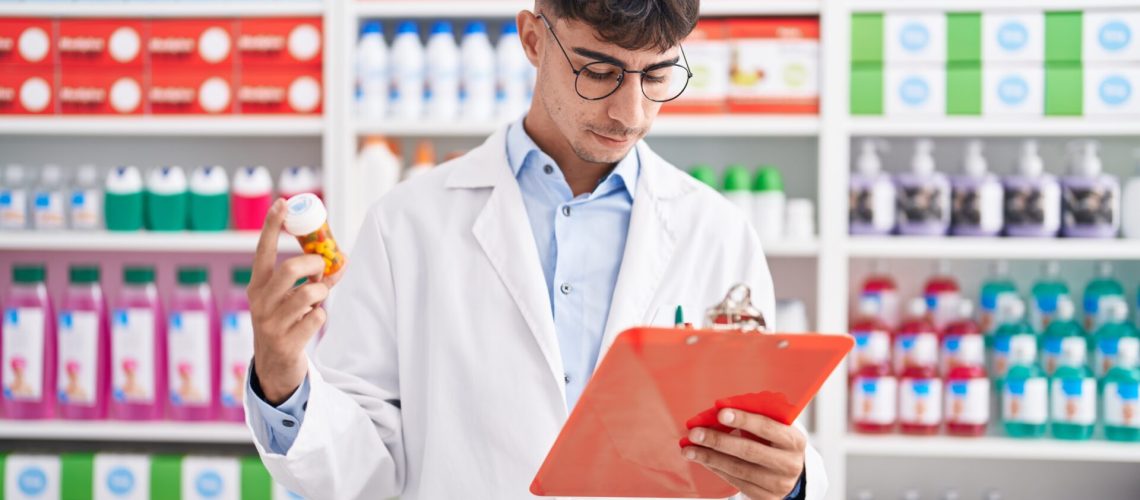 Young hispanic man pharmacist holding pills bottle reading document at pharmacy